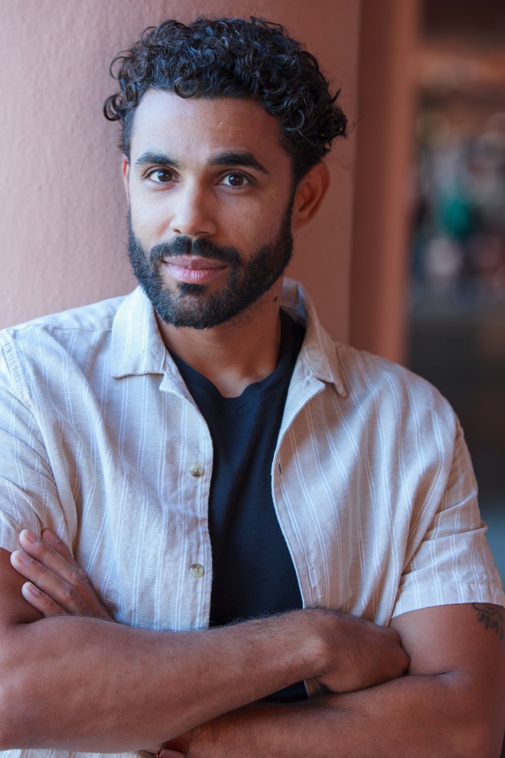 Headshot, arms crossed, in front of a rose-colored wall