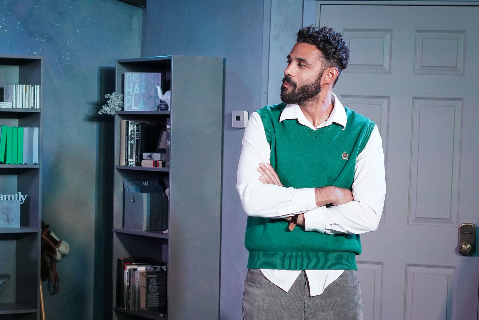 Howie in a green sweater vest, arms crossed, in Rabbit Hole