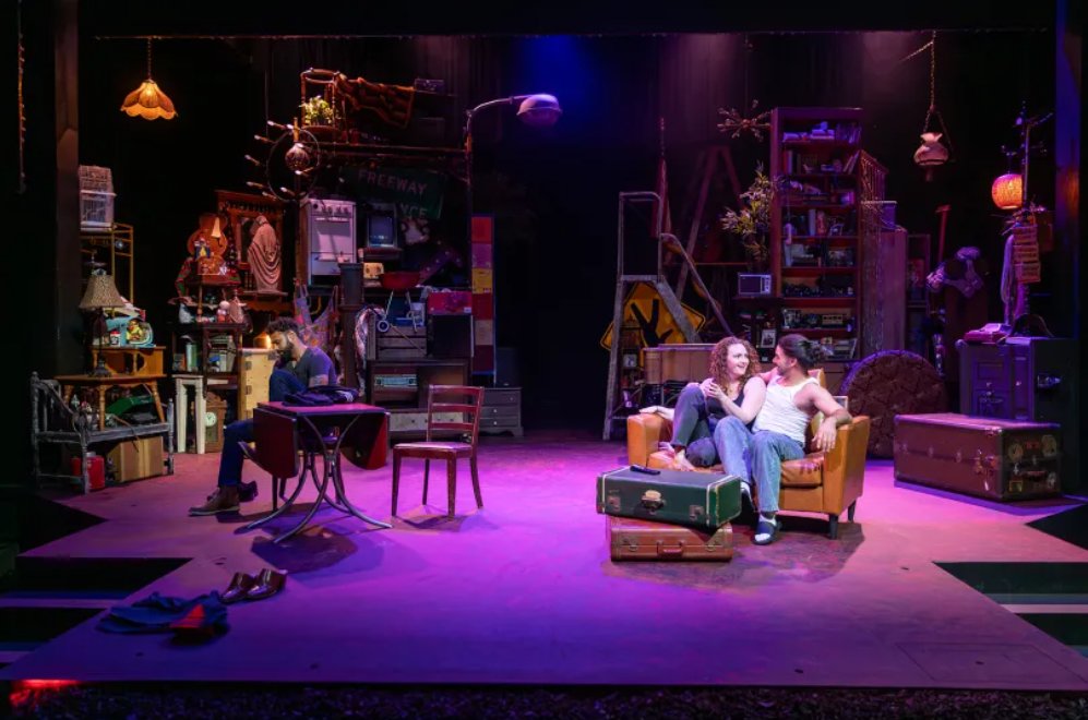 Full stage view of The Strangers, with Niegel seated at a table on the left